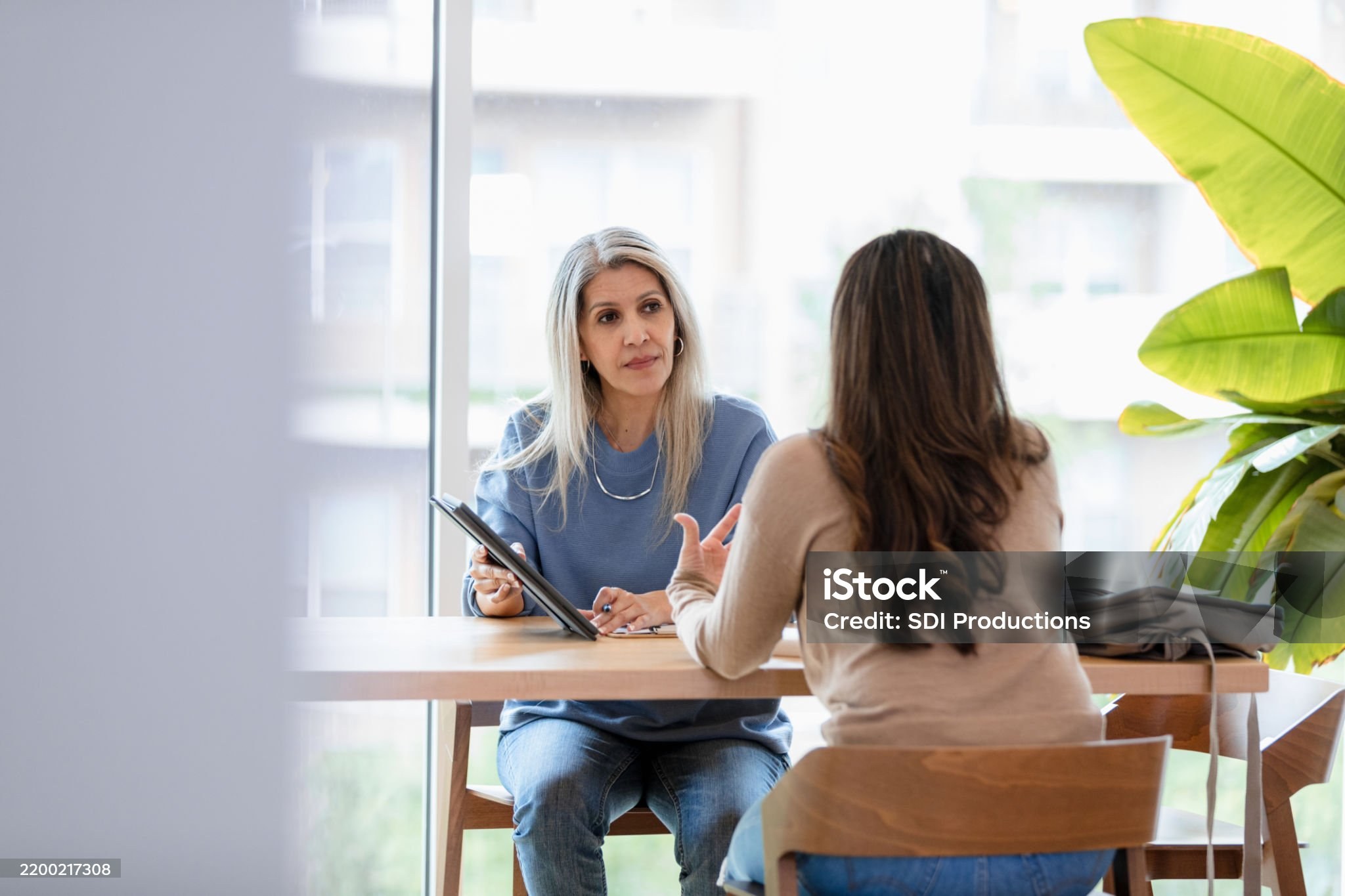 Two women in casual wear having a discussion using a tablet during a meeting.