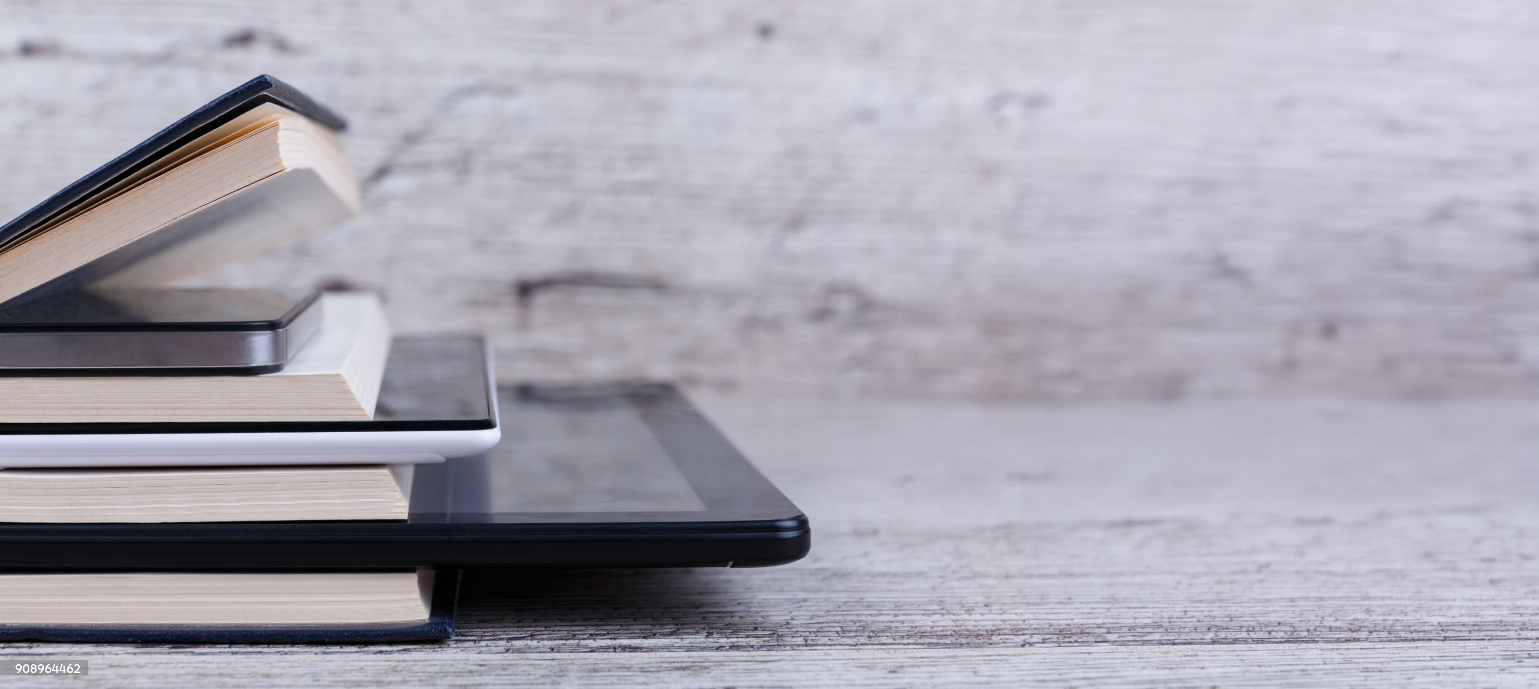 Various modern tablets are among a stack of different books. On a wooden background. The concept of knowledge. Close-up.