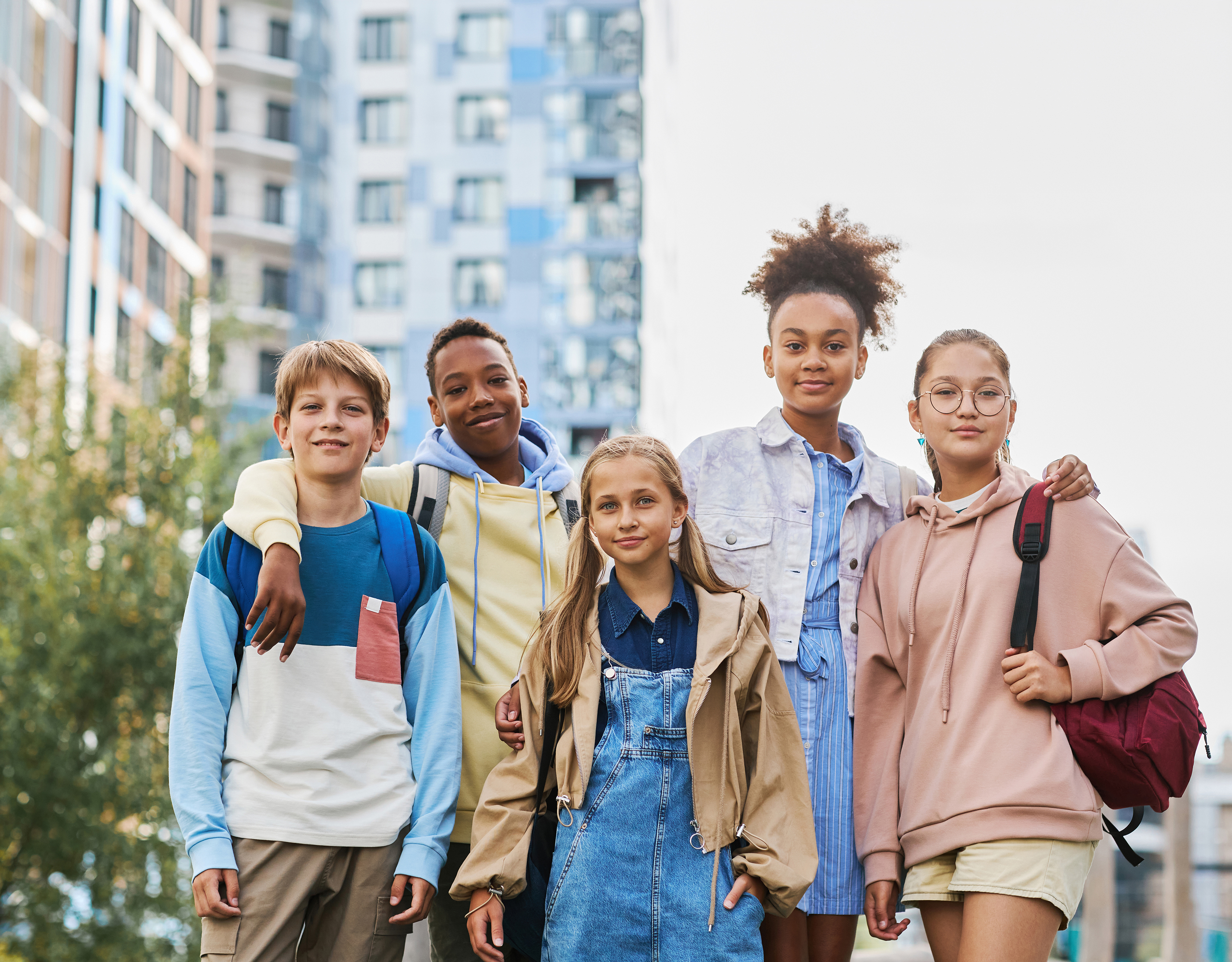 Group of five multicultural secondary school learners in casualwear standing in row in urban environment and looking at camera