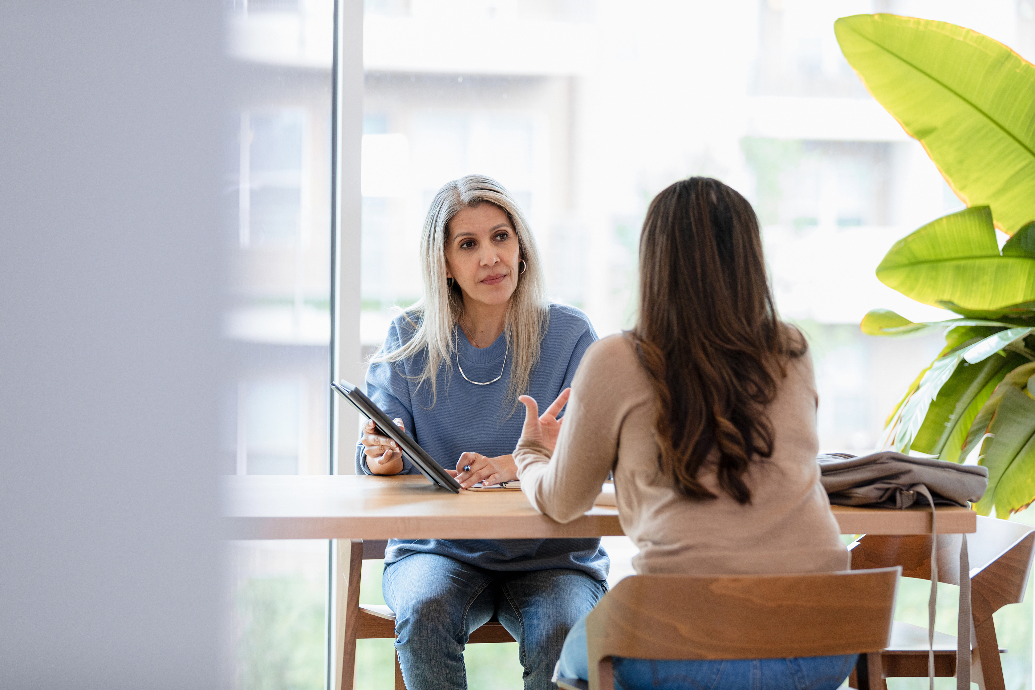 Two women in casual wear having a discussion using a tablet during a meeting.