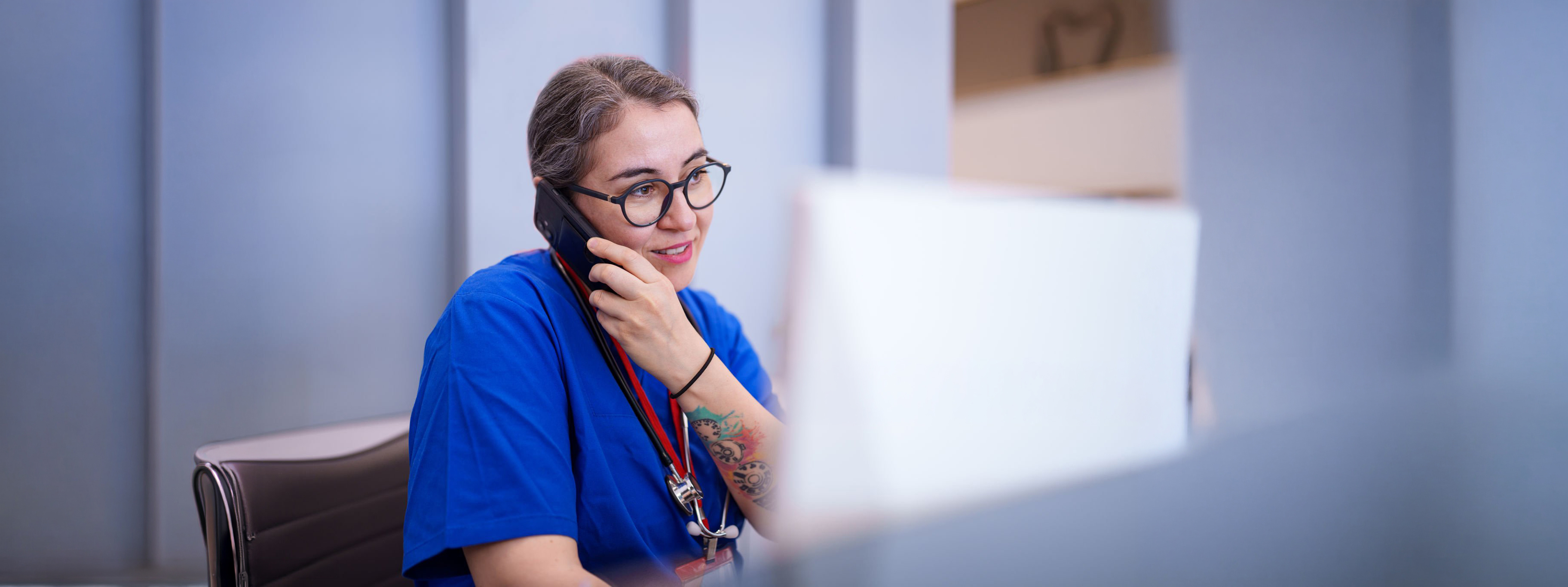 A healthcare worker sits at a desk, engaged in a conversation on the phone. The scene highlights the essential communication and administrative tasks healthcare professionals handle in a clinical environment.