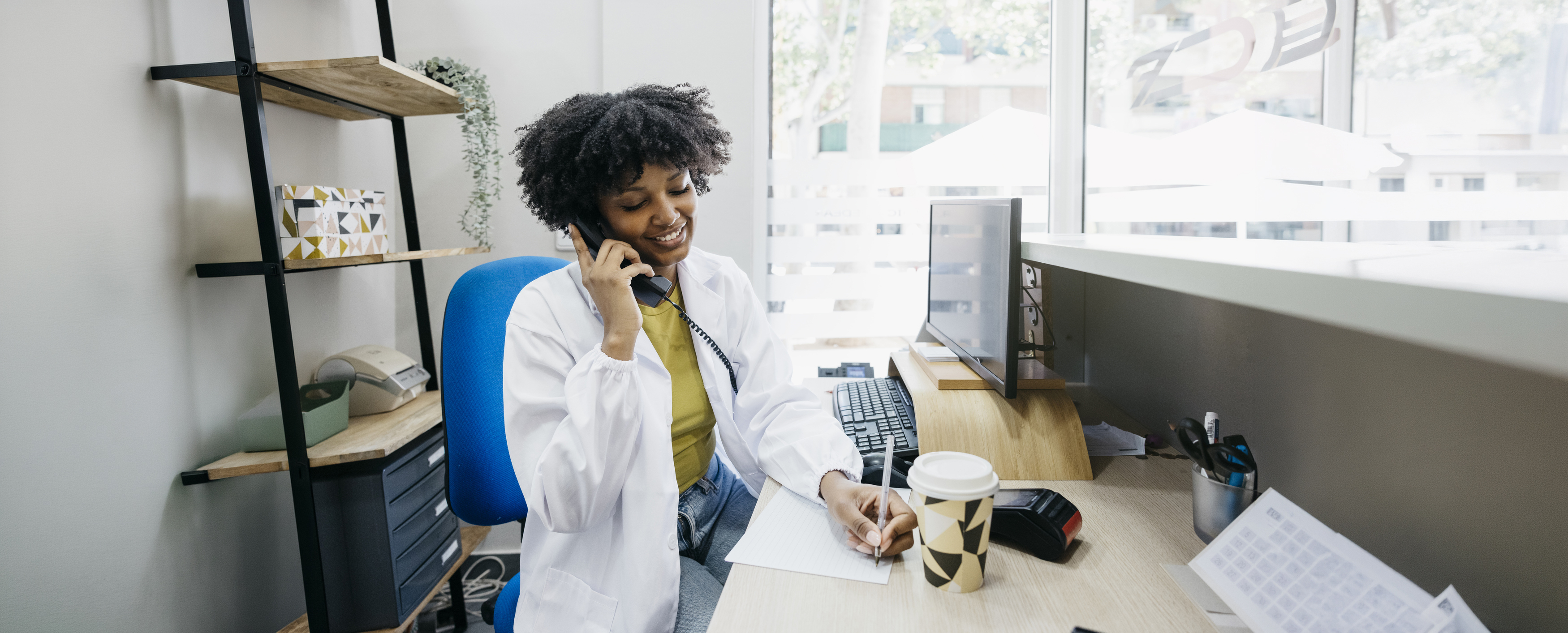 Friendly medical receptionist taking notes while talking on the phone