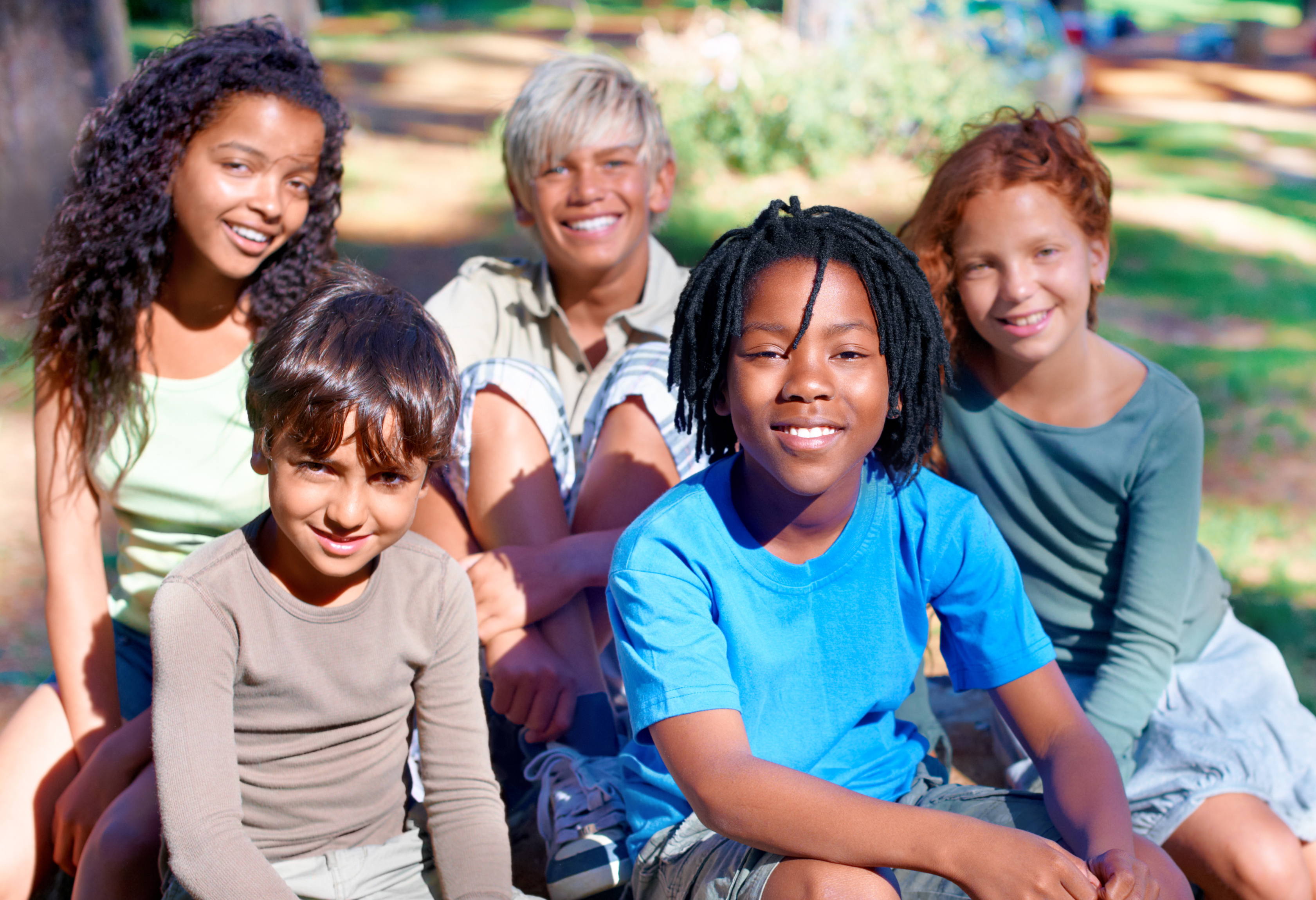 A group of children smiling at the camera in the outdoors.