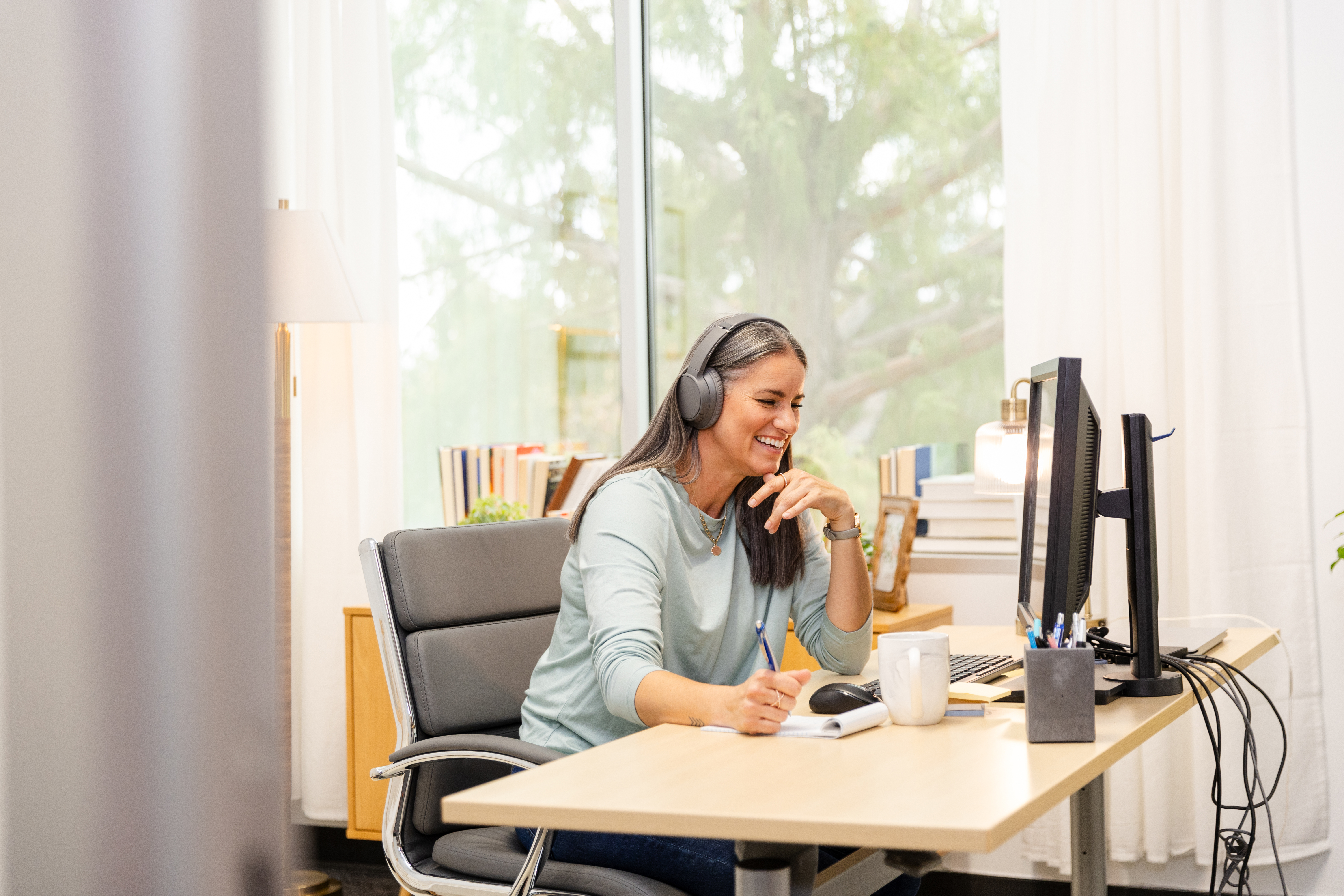 Happy mid adult woman works from home office using computer.  Casual, wireless technology.
