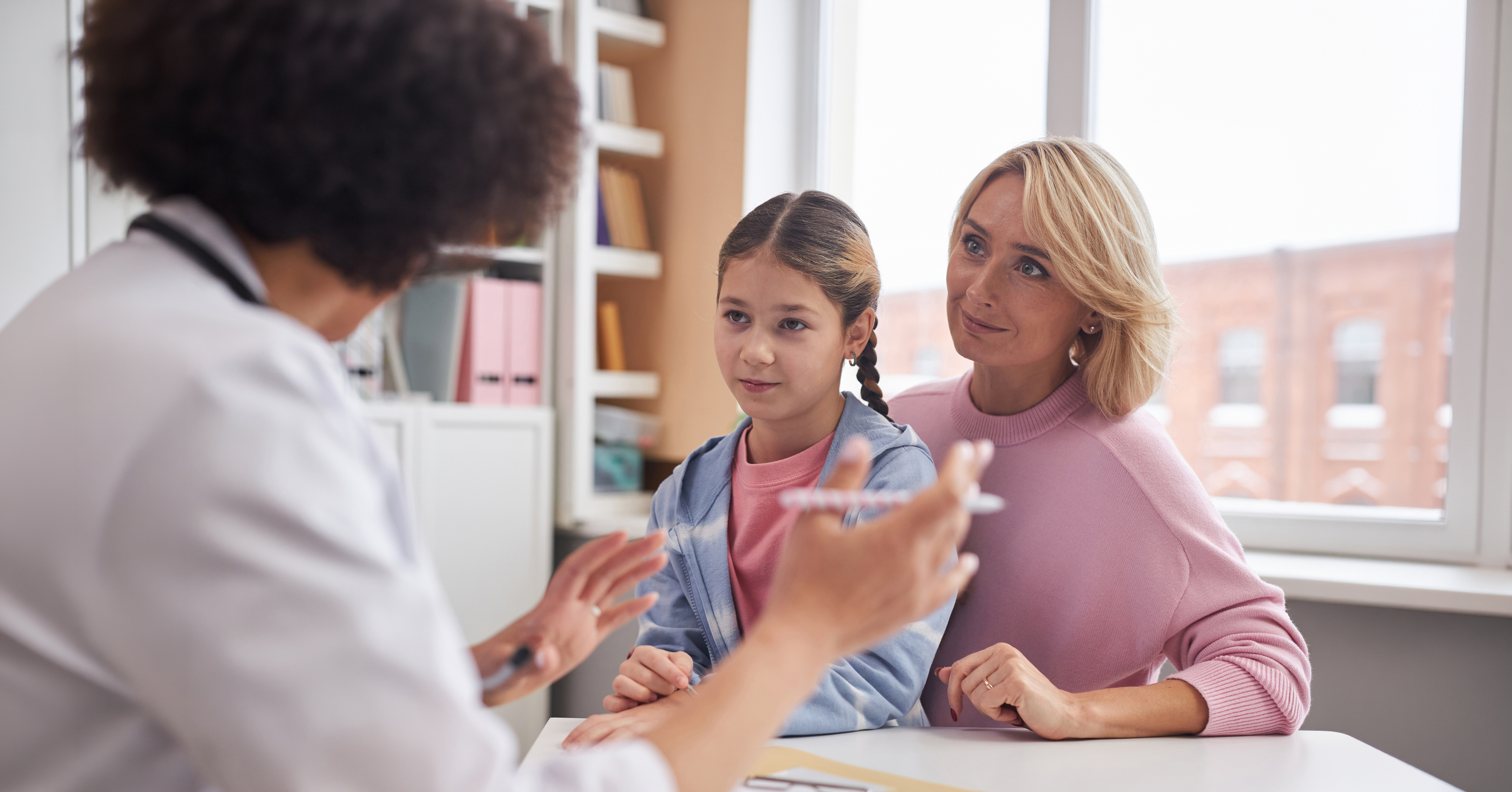 Portrait of Caucasian mother and daughter listening to pediatrician while visiting doctor in clinic