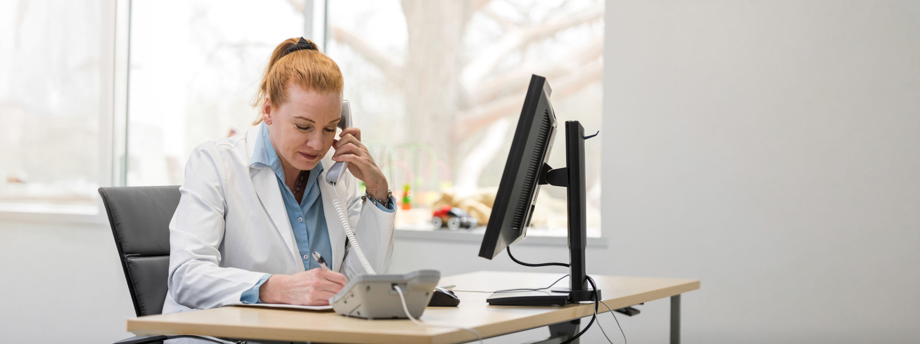 The mature adult female pediatrician uses the landline phone in her office to confirm a patient's test results.