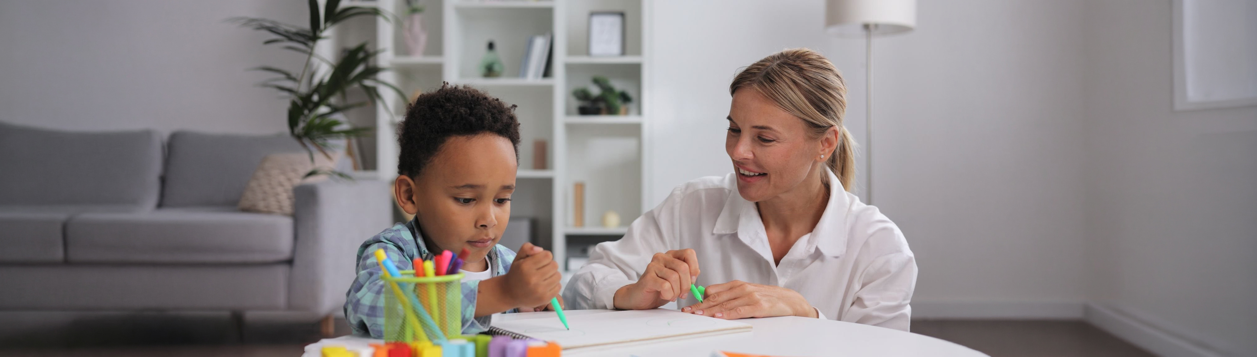Adorable little african american boy with curly hair having fun at pediatric specialist appointment, happy child drawing with female therapist, exercises for children with autism.